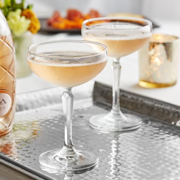 A tray holding two Acopa Empire coupe glasses of champagne.