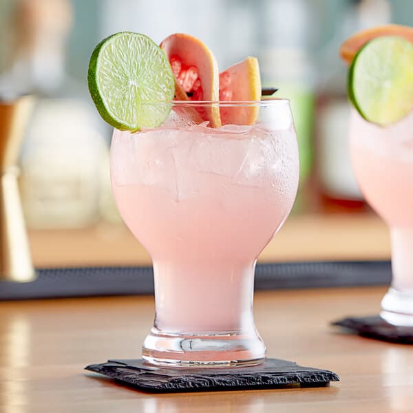 Two Acopa Select Craft Master glasses filled with pink drinks and fruit slices on a table in a cocktail bar.