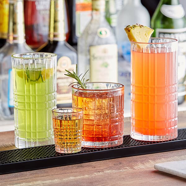 A row of Acopa Madras highball glasses filled with different colored drinks on a bar.