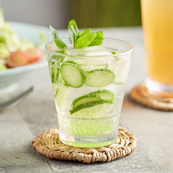 An Acopa Endure Tritan plastic rocks glass of water with cucumber slices and mint leaves.