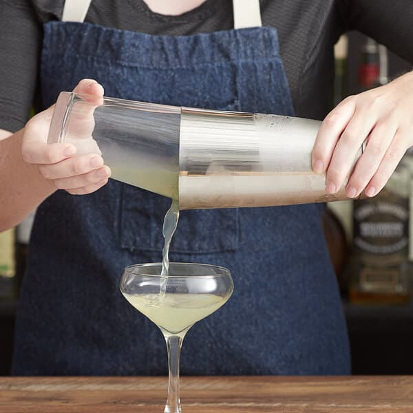 A person using an Acopa stainless steel cocktail shaker to pour a drink.