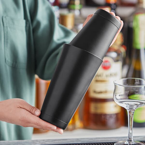A person holding a black Acopa Boston shaker set on a counter in a cocktail bar.