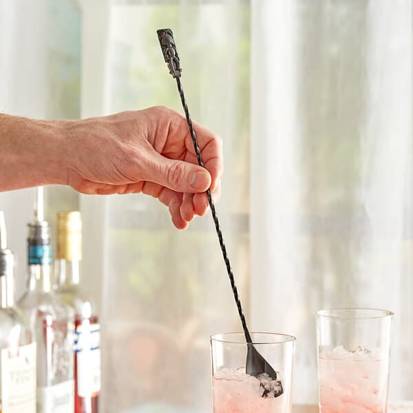 A hand using an Acopa black weighted bar spoon with a tiki end to stir a drink with ice.