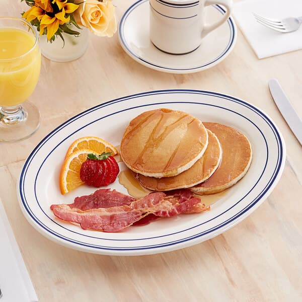 An Acopa ivory stoneware platter with pancakes, bacon, and orange slices.