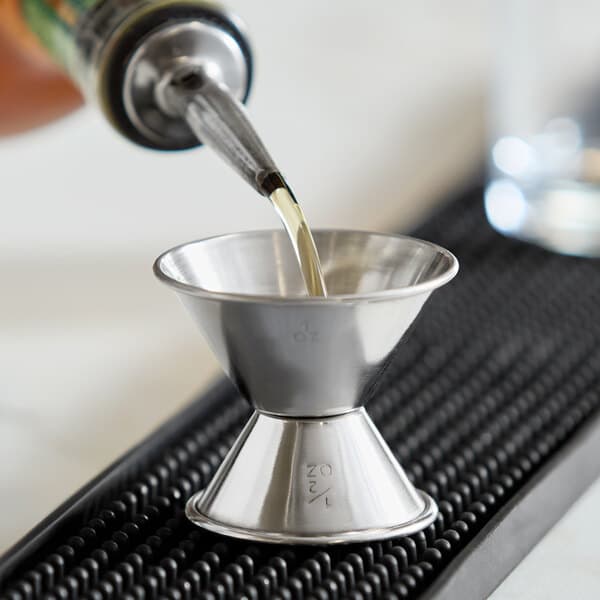 A stainless steel jigger with 0.5 oz. and 1 oz. measurement markings being used to pour liquid.
