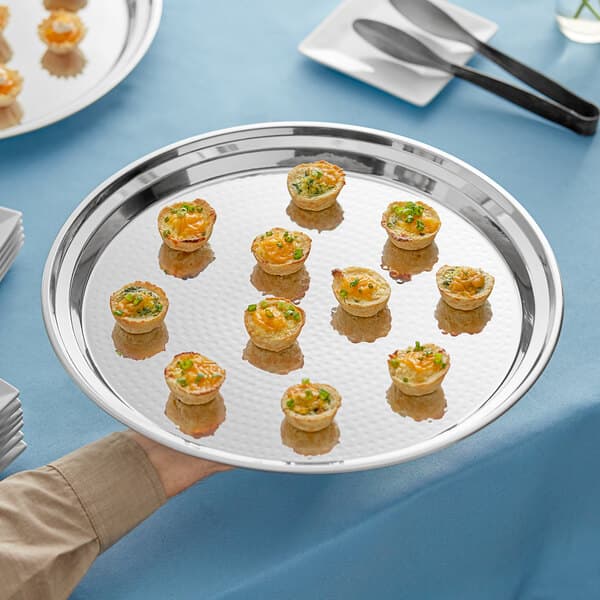 A person's hand holding an Acopa stainless steel catering tray of small food.