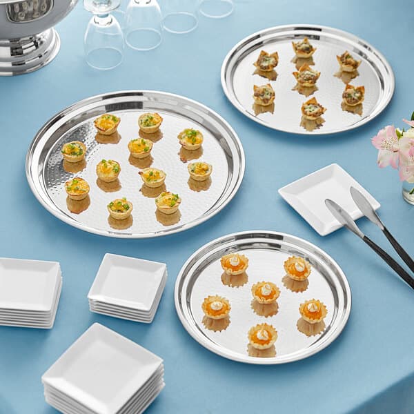 A group of Acopa stainless steel platters and white plates with food on them.