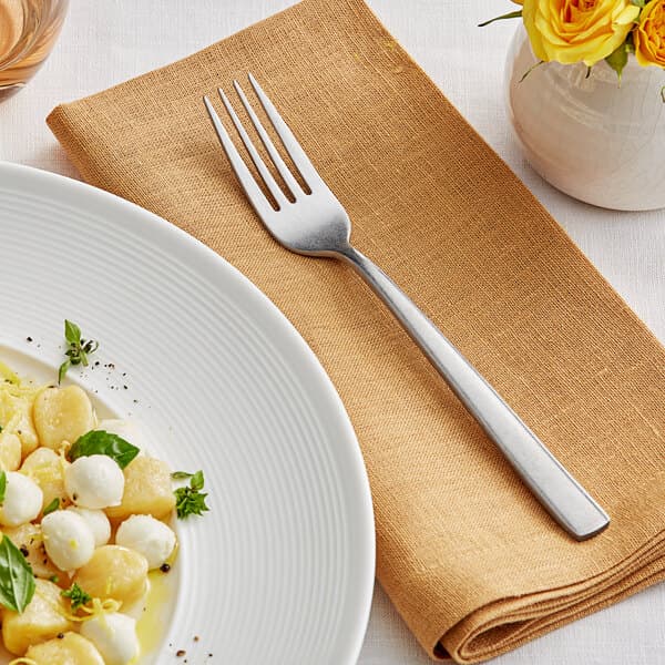 A plate of pasta with an Acopa Petra dinner fork on a placemat.