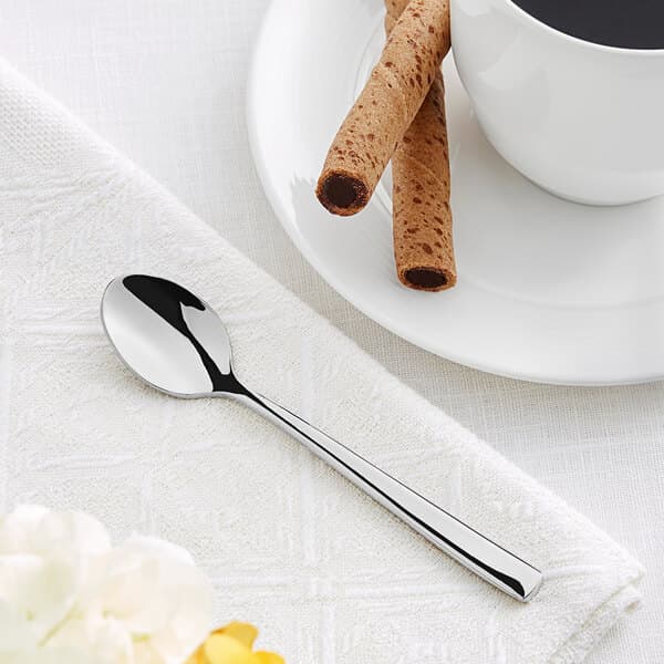 An Acopa stainless steel demitasse spoon on a white napkin next to a cup of coffee.