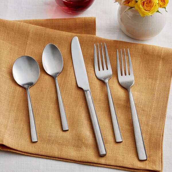 Acopa Petra stainless steel flatware on a napkin with yellow flowers.