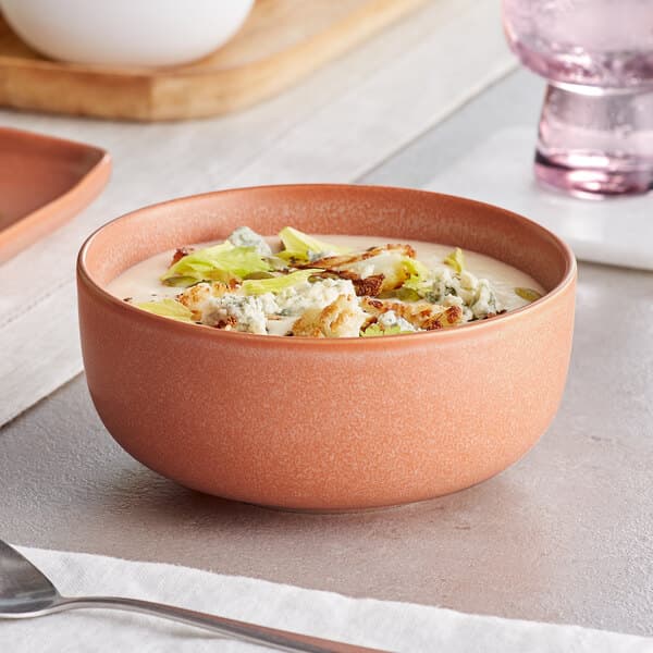A Terra Cotta matte porcelain bowl filled with soup and vegetables on a table.