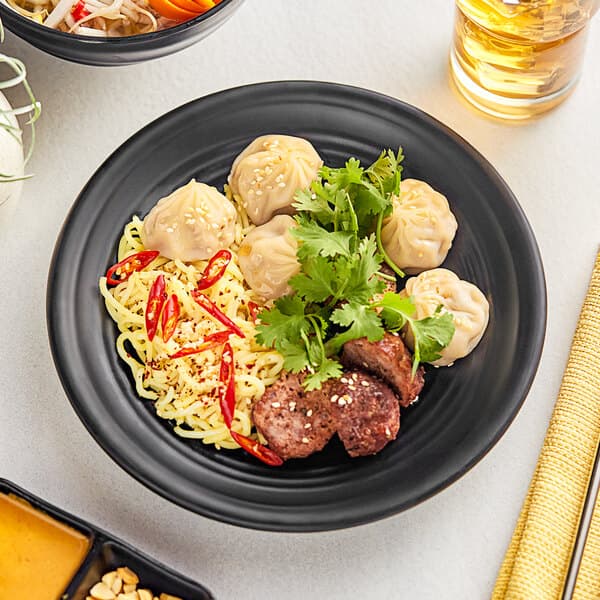 A plate of food with noodles, meat, and vegetables on an Acopa Izumi matte black melamine plate.