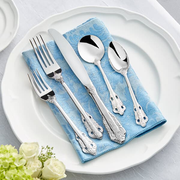 A white plate with Acopa Ophelia stainless steel flatware on a blue towel.