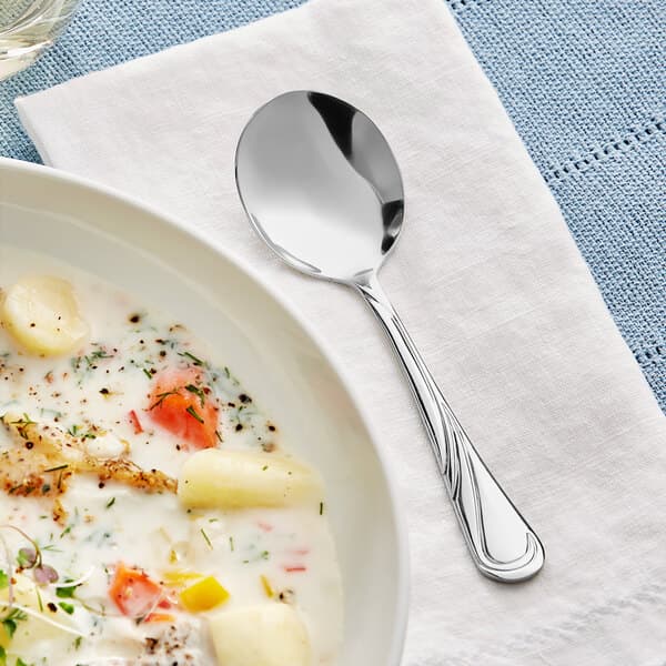 An Acopa stainless steel bouillon spoon in a bowl of soup.