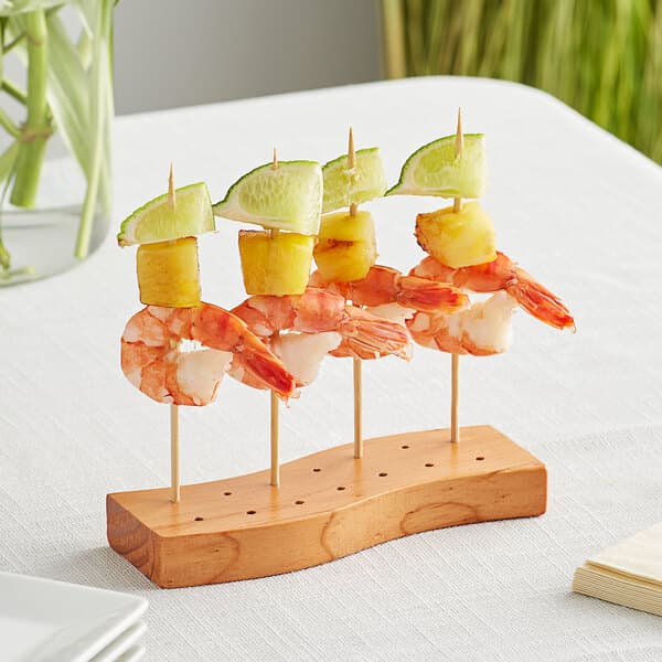 An Acopa dark brown wood skewer holder with fruit on skewers.