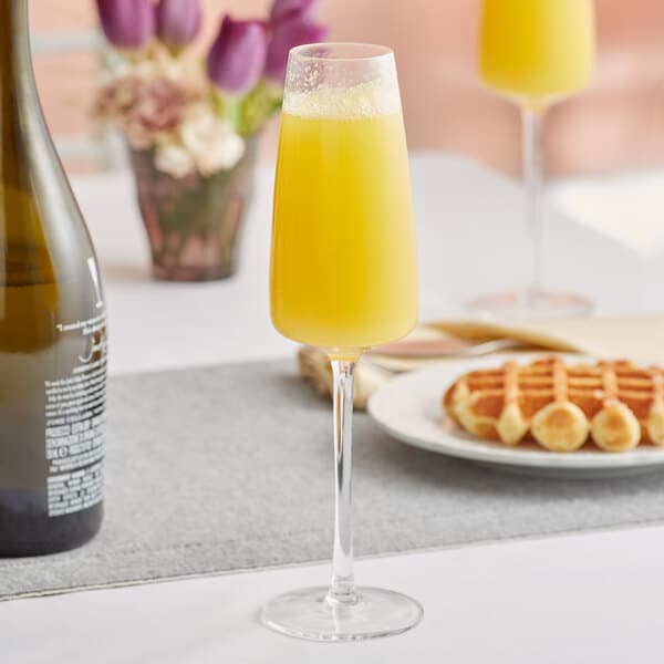A close-up of an Acopa Piatta flute glass filled with yellow liquid on a table.