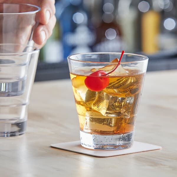A close-up of a hand holding an Acopa Select clear flared rocks glass with ice and a cherry.