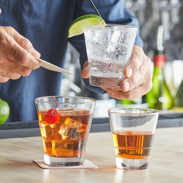 A man holding an Acopa Select flared rocks glass filled with liquid and ice with a cherry and a lime wedge.