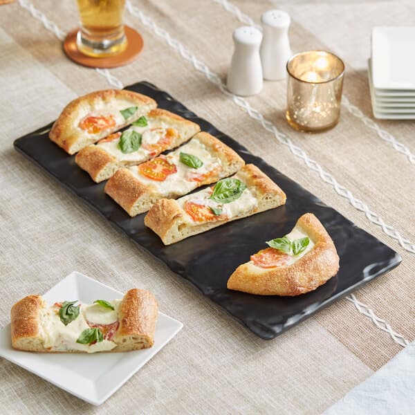 An Acopa faux slate melamine serving board with pizza slices on it on a table.