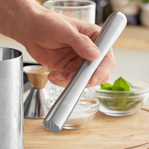 A hand holding an Acopa brushed stainless steel muddler with a tenderizer head.