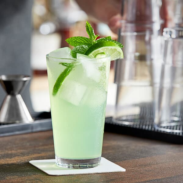 A person holding an Acopa Select stackable beverage glass filled with a green drink and lime slices.