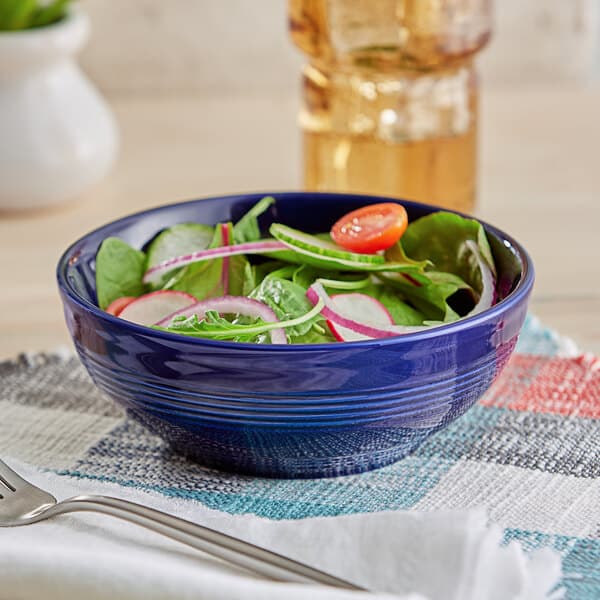 A bowl of salad with vegetables in an Acopa Capri deep sea cobalt bistro bowl.