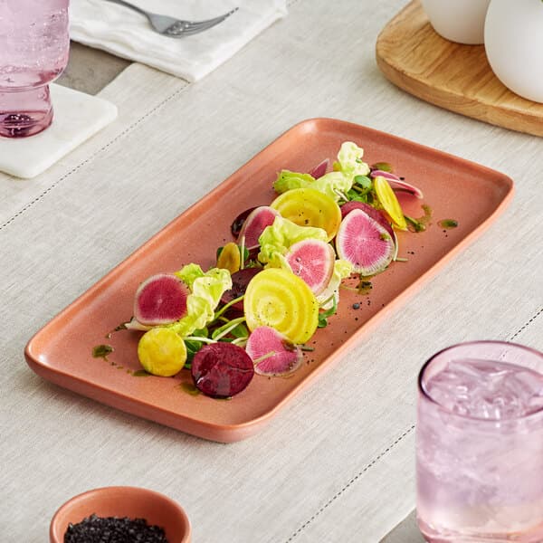A rectangular Acopa Terra Cotta porcelain platter with a radish salad on a table.