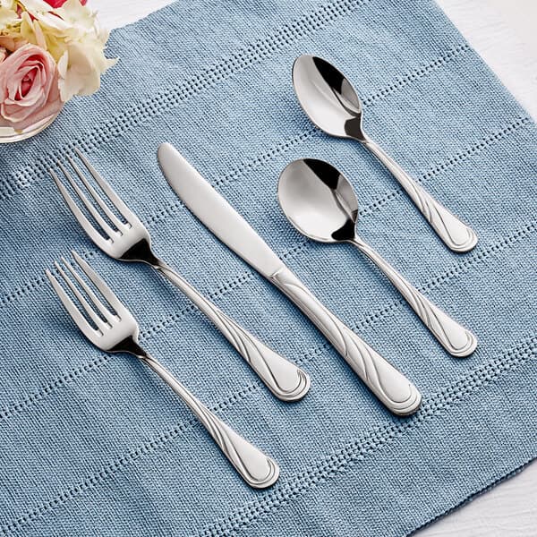 Acopa Swirl stainless steel flatware set on a blue cloth with a napkin.