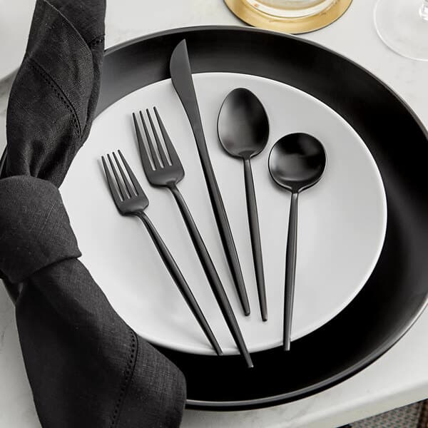 A white plate with a black Acopa Odin flatware set consisting of a knife, fork, and spoon.
