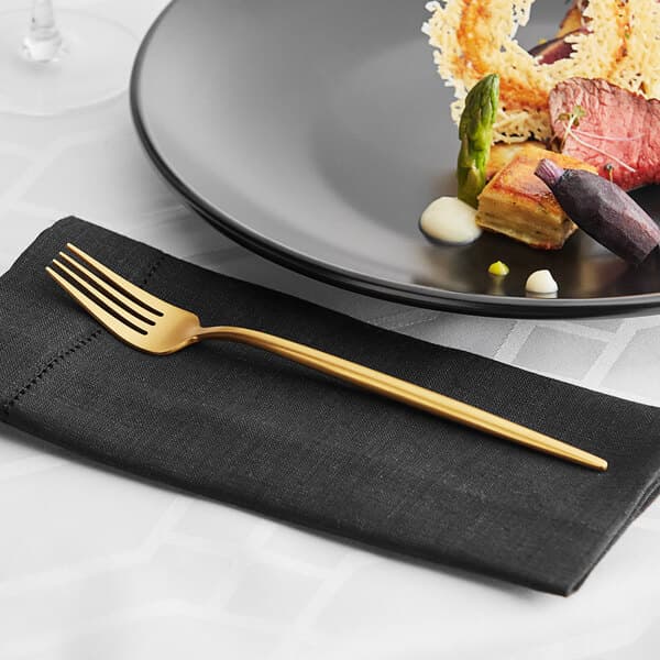 An Acopa Odin brushed stainless steel dinner fork on a napkin next to a plate of food.