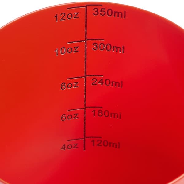 An Acopa red frothing pitcher with black measuring lines on a counter.