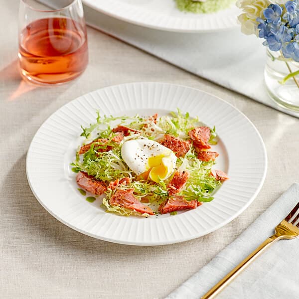 A plate of salad with a fork on a Cordelia wide rim porcelain plate on a table.