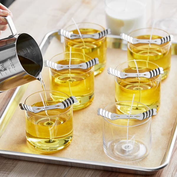 A tray of Acopa cylindrical glass candle holders filled with yellow liquid.