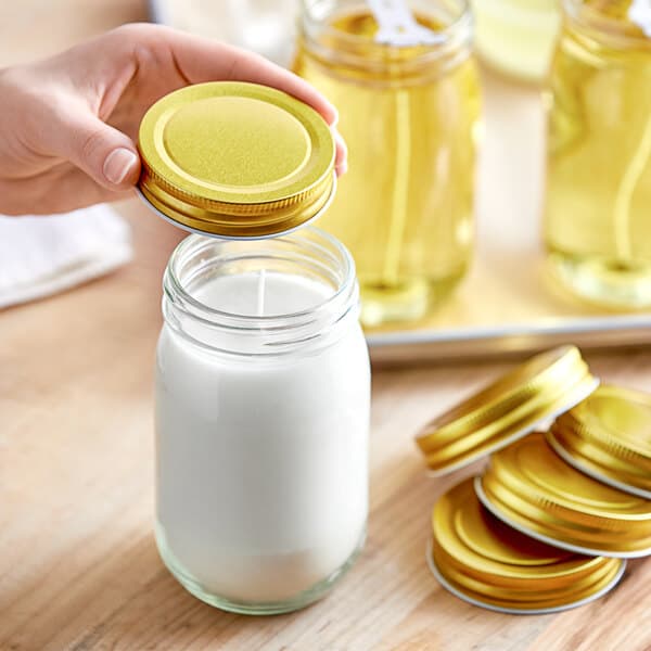 A person's hand holding a gold lid over a glass jar.