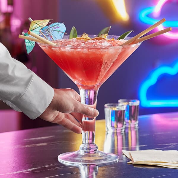 A bartender holding an Acopa Colossal martini glass with a red drink.
