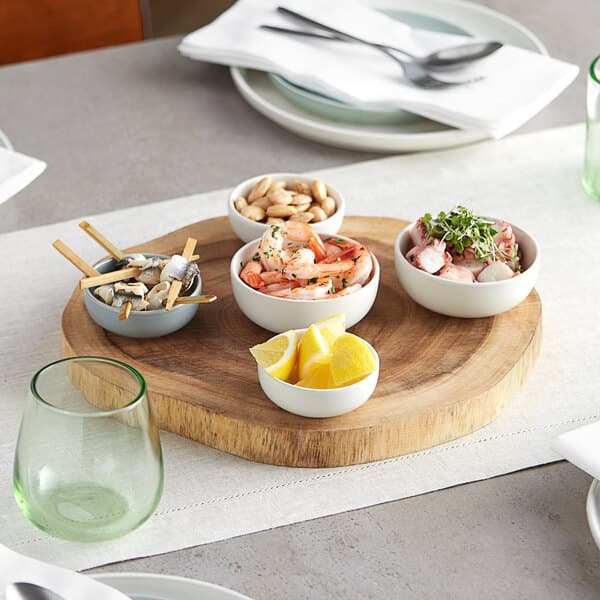 An Acopa round acacia wood serving board with bowls of food on it.