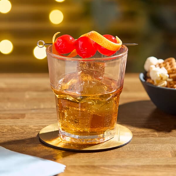 An Acopa Memphis rocks glass of whiskey with ice and fruit on a table with a bowl of popcorn and nuts.