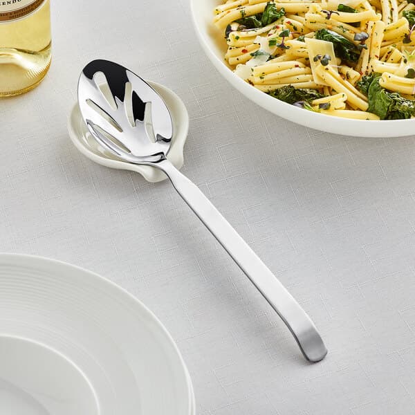 An Acopa stainless steel slotted serving spoon in a dish of pasta.
