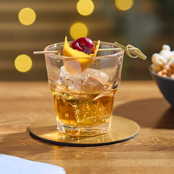 A Memphis old fashioned glass with ice and a cherry on a gold coaster.