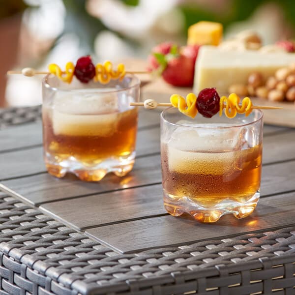 Two Acopa Tritan plastic rocks glasses with drinks and cheese on a table.