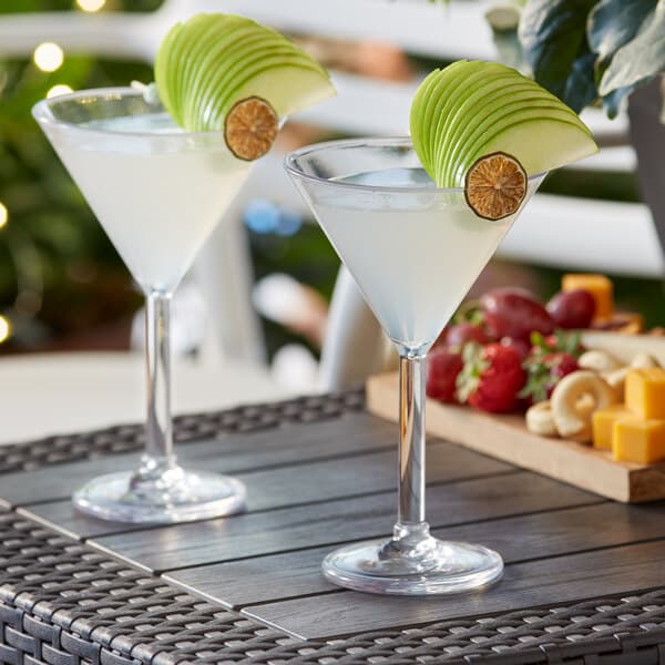 Two Acopa Endure plastic martini glasses filled with liquid and fruit on a table.