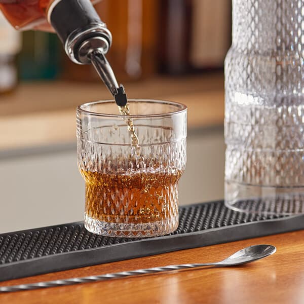 A person pouring whiskey into an Acopa stackable rocks glass on a counter in a cocktail bar.