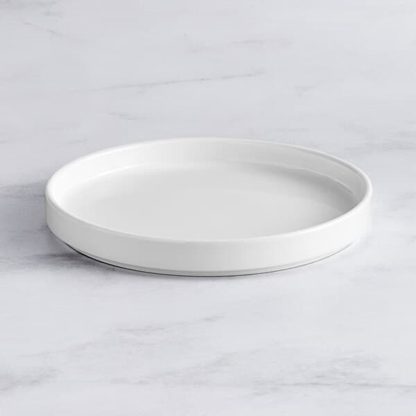 An Acopa Lore bright white porcelain plate with a raised rim on a marble surface.