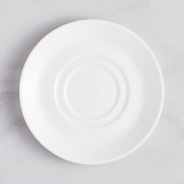 An Acopa Lore bright white porcelain saucer with a circular pattern on a marble surface.