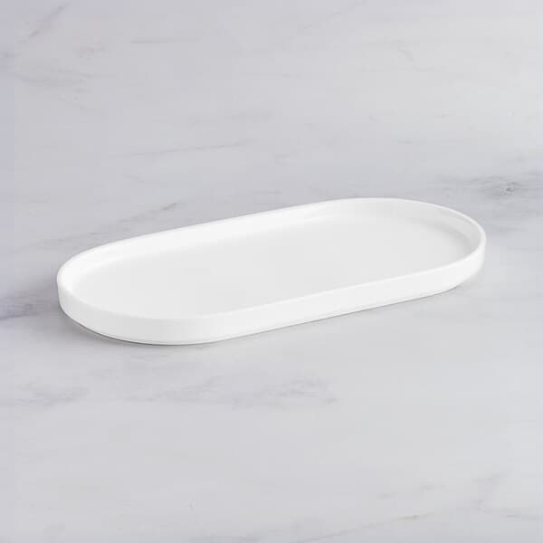 An Acopa Lore bright white porcelain rectangular platter with raised edges on a marble surface.