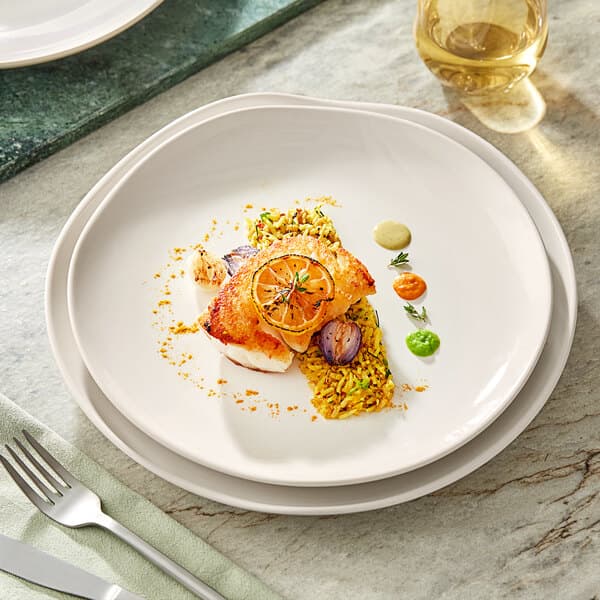 A Acopa Highlands white coupe china plate with food and a fork on a table.