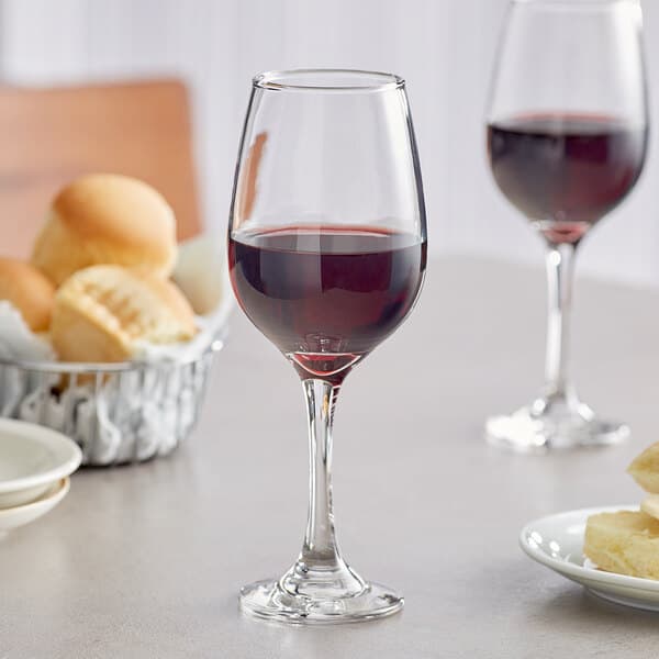 An Acopa wine glass filled with red wine on a table with bread.