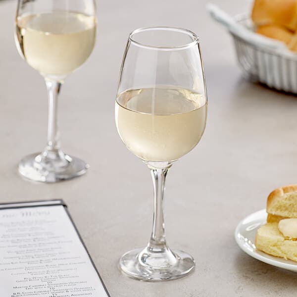Two Acopa all-purpose wine glasses filled with white wine next to a plate of food
