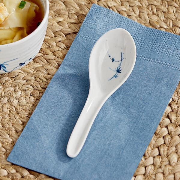 An Acopa Biru melamine wonton soup spoon on a cloth next to a bowl of soup.