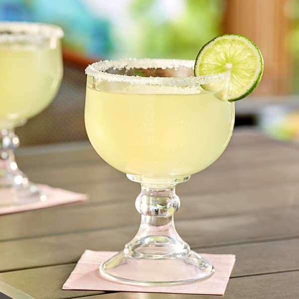 Two Acopa schooner glasses with yellow liquid and a lime slice on top on a table outdoors.